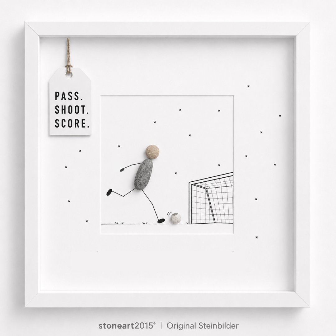 Steinbild mit einem Fußballspieler aus Kieselsteinen, der einen Ball auf ein gezeichnetes Tor schießt, Schriftzug Pass Shoot Score