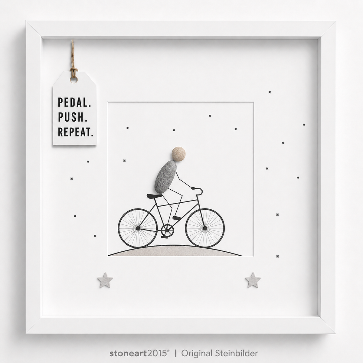 Steinbild mit einem Radfahrer aus Kieselsteinen auf einem gezeichneten Fahrrad, kleine Sterne, Schriftzug Pedal Push Repeat