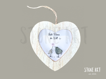 Dekoratives Steinbild mit der Aufschrift „Beste Mama der Welt“, gestaltet in einem herzförmigen Rahmen aus Treibholz-Optik, verziert mit kleinen Natursteinen, die zwei stilisierte Figuren darstellen. Ideal zum Aufhängen als liebevolles Geschenk zum Muttertag oder als Dankeschön.