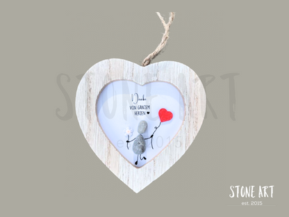 Steinbild mit der Aufschrift „Danke von ganzem Herzen“ in einem herzförmigen Holzrahmen. Zwei stehende Figuren aus Kieselsteinen mit einem roten Herz darüber. Handgefertigte Wanddekoration zum Aufhängen.