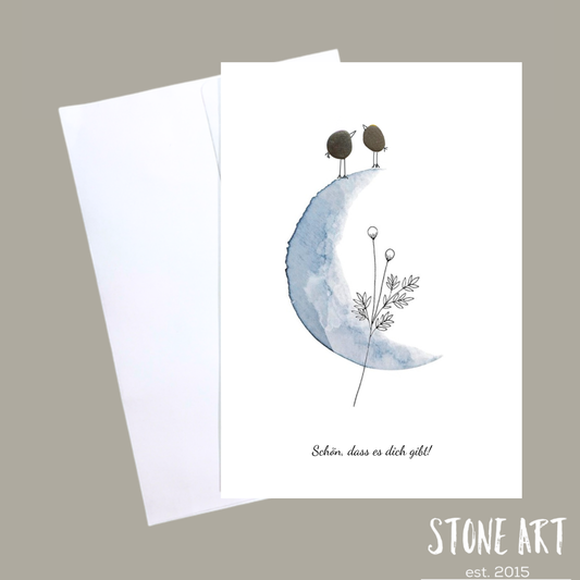 Minimalistische Karte mit zwei aus Kieselsteinen arrangierten Vögelchen und dem Schriftzug ‚Schön, dass es dich gibt‘.