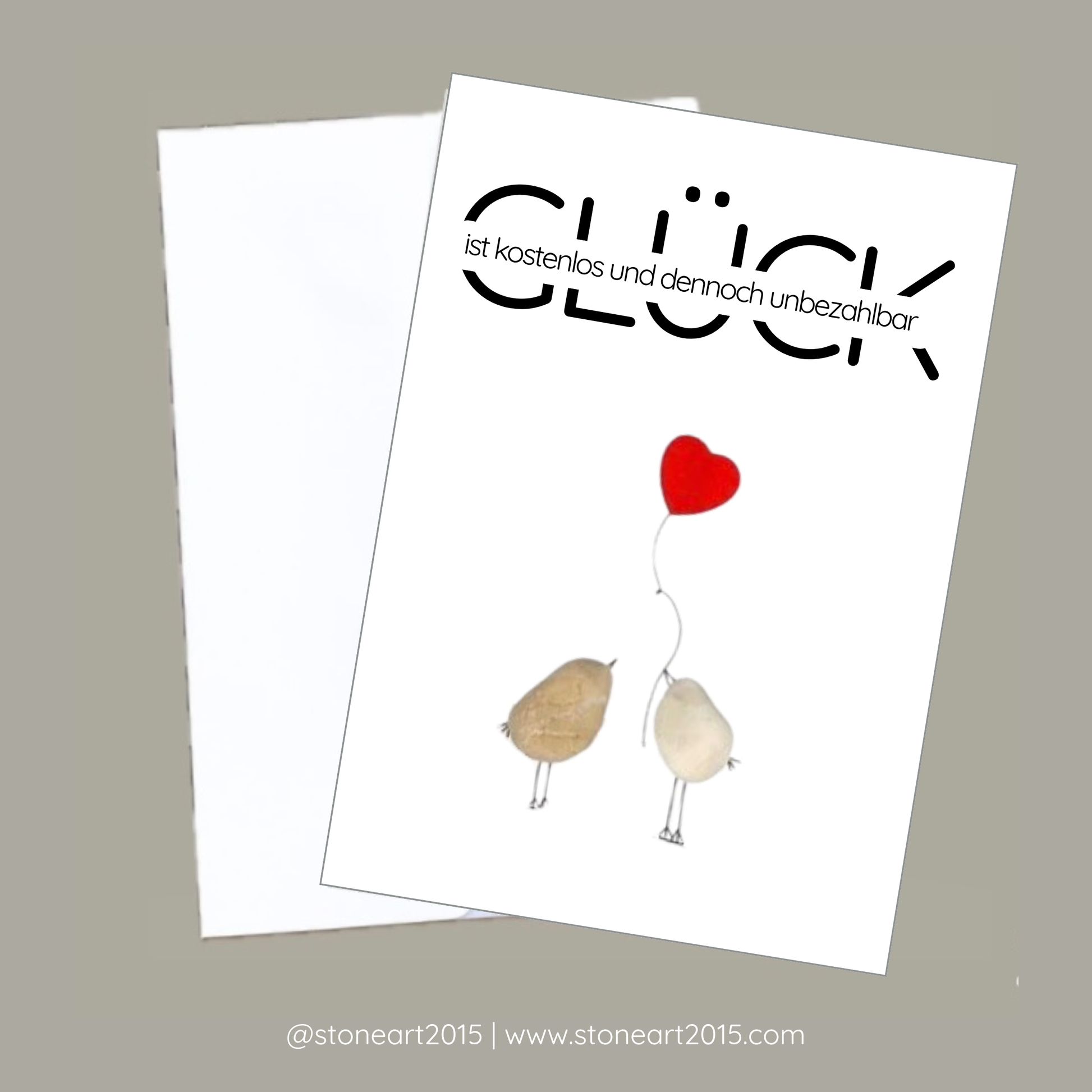 Inspirierende Karte mit zwei aus Kieselsteinen gestalteten Vögelchen und dem Spruch ‚Glück ist kostenlos und dennoch unbezahlbar‘