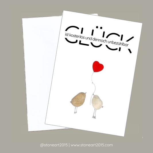 Inspirierende Karte mit zwei aus Kieselsteinen gestalteten Vögelchen und dem Spruch ‚Glück ist kostenlos und dennoch unbezahlbar‘