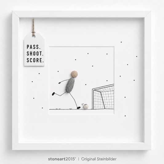 Steinbild mit einem Fußballspieler aus Kieselsteinen, der einen Ball auf ein gezeichnetes Tor schießt, Schriftzug Pass Shoot Score