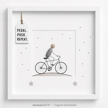 Steinbild mit einem Radfahrer aus Kieselsteinen auf einem gezeichneten Fahrrad, kleine Sterne, Schriftzug Pedal Push Repeat