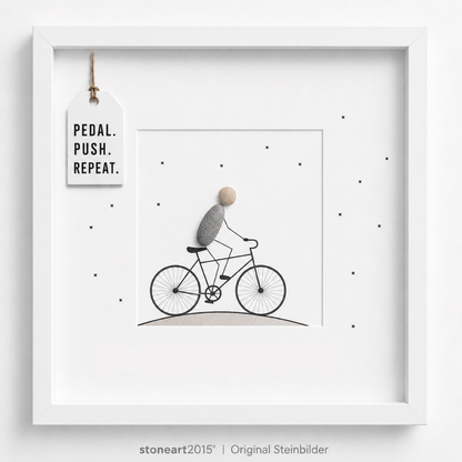 Steinbild mit einem Radfahrer aus Kieselsteinen auf einem gezeichneten Fahrrad, kleine Sterne, Schriftzug Pedal Push Repeat