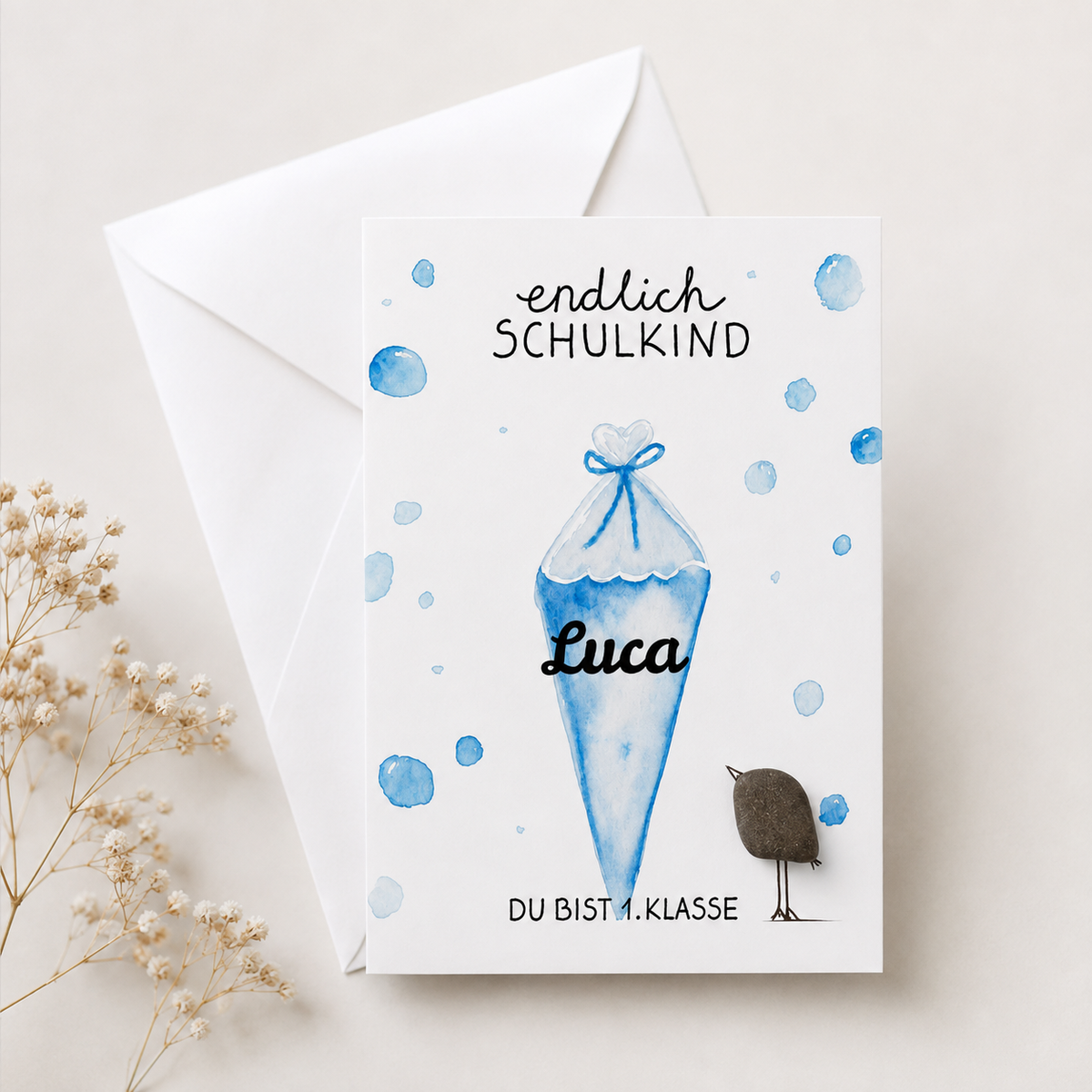 Handgemachte weiße Klappkarte mit Kieselstein-Vogel und blauer Aquarell-Schultüte, personalisiert mit Namen, Spruch „endlich Schulkind – du bist 1. Klasse“ – Einschulungskarte, Grußkarte mit Umschlag